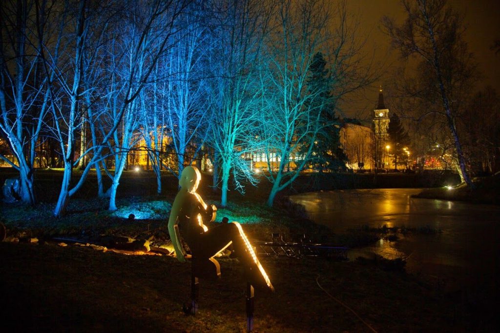 Illuminated figure on the river bank, illuminated trees in the background